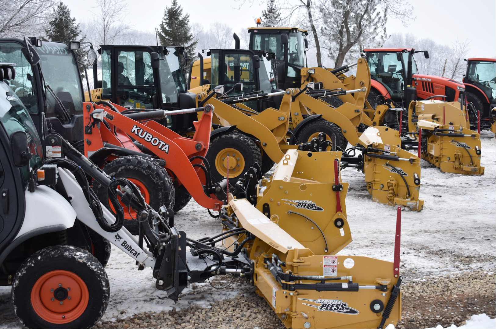 Several Metal Pless snow plows on the front of snow removal machines